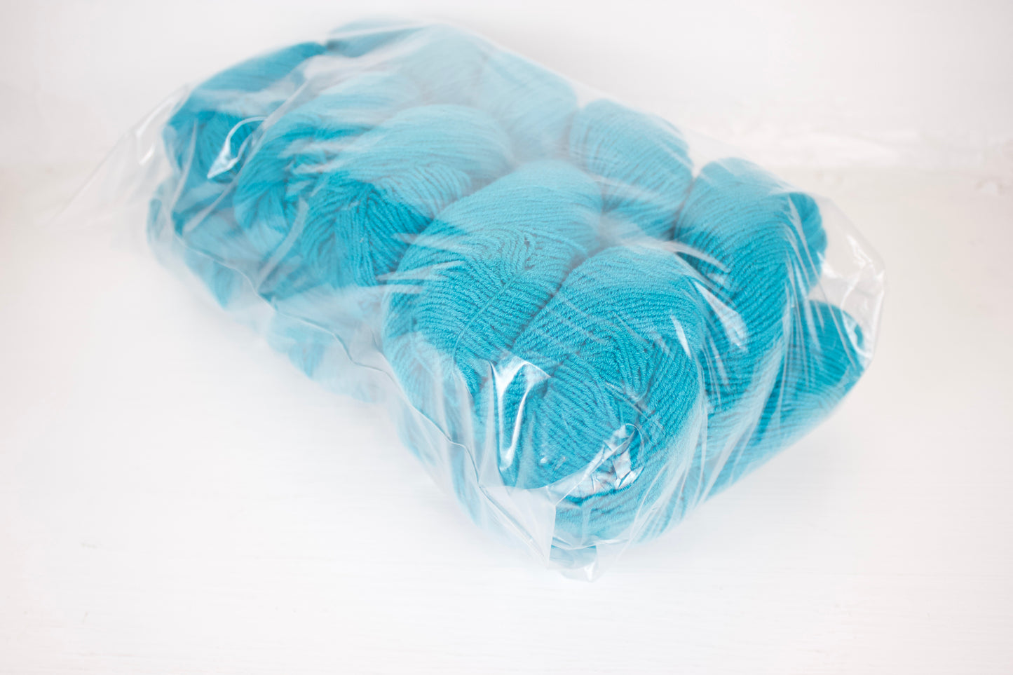 Ten skeins of blue yarn in a clear plastic bag on a white background