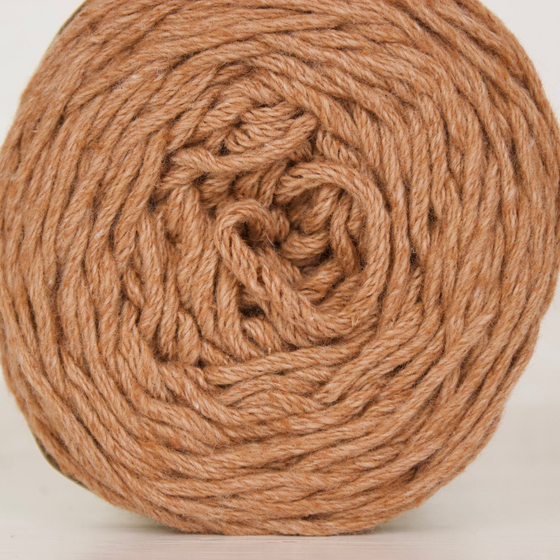 A ball of natural brown cotton yarn wound in a spiral pattern, shown against a plain white background.
