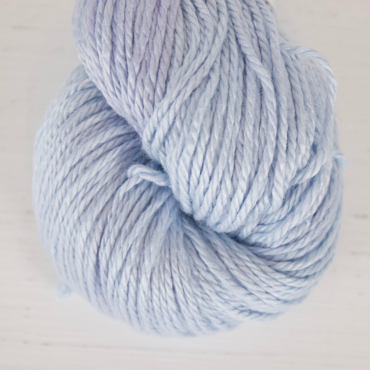 A skein of light periwinkle blue yarn resting on a white wooden surface.