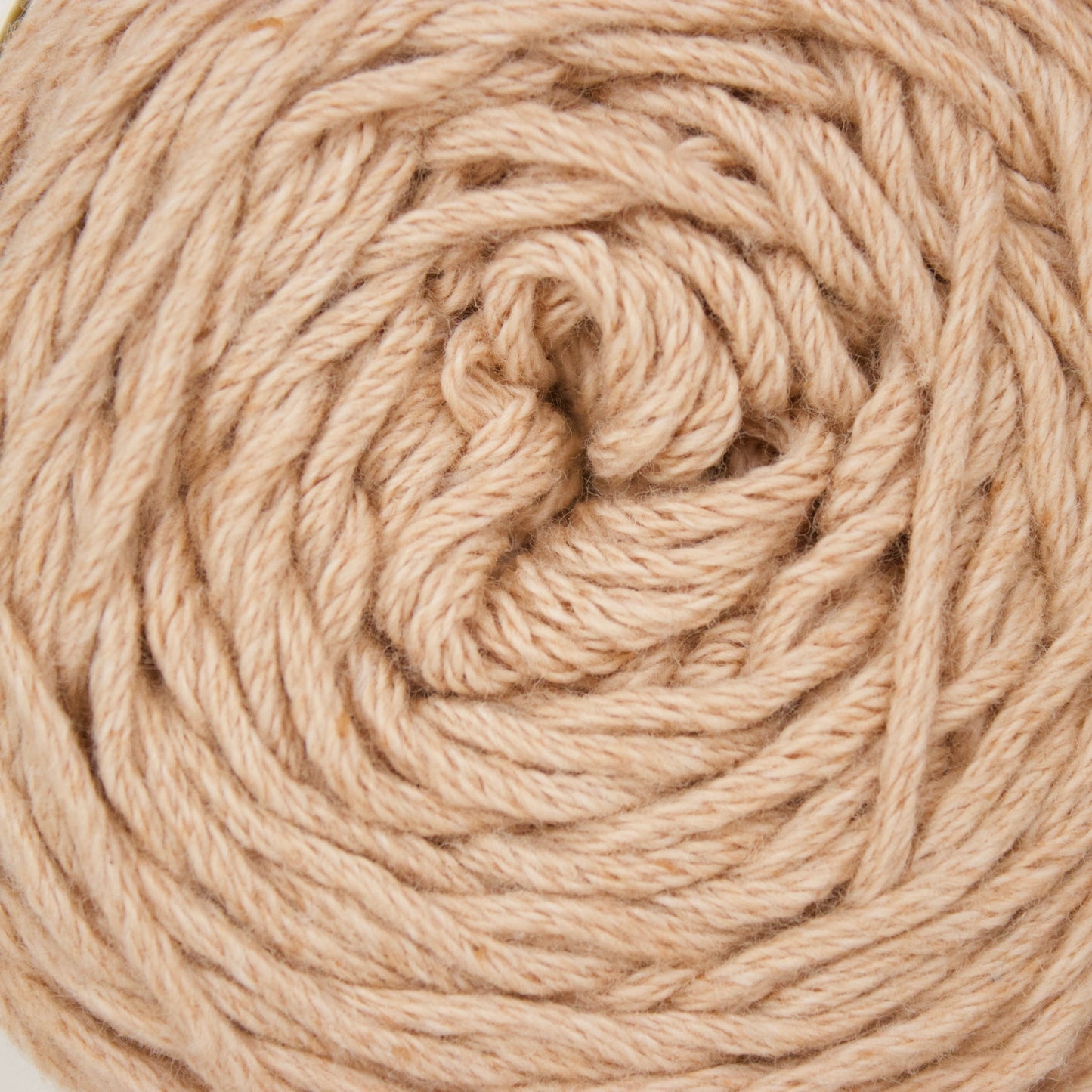 A close-up of a coiled ball of natural beige cotton yarn against a plain white background.