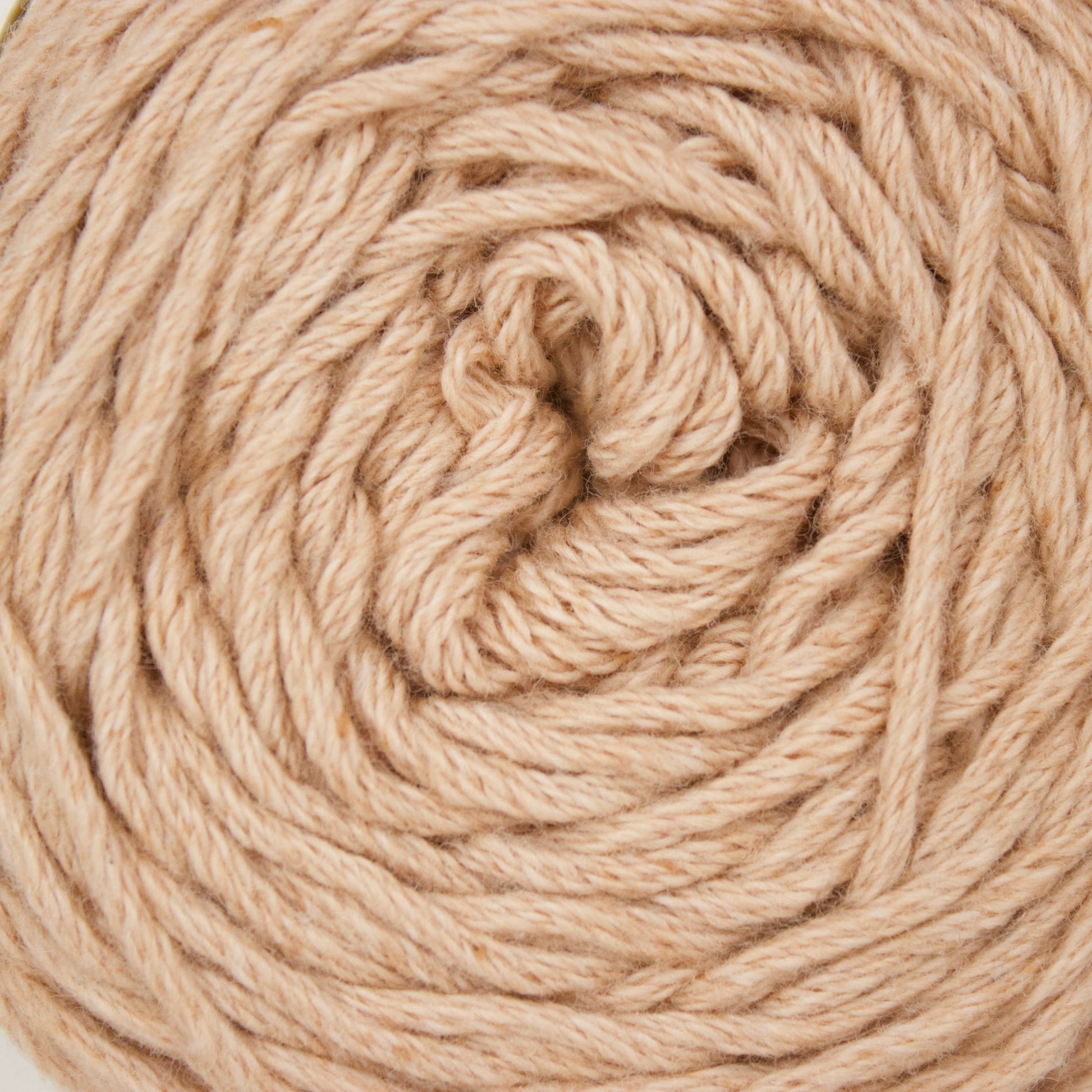 A close-up of a coiled ball of natural beige cotton yarn against a plain white background.