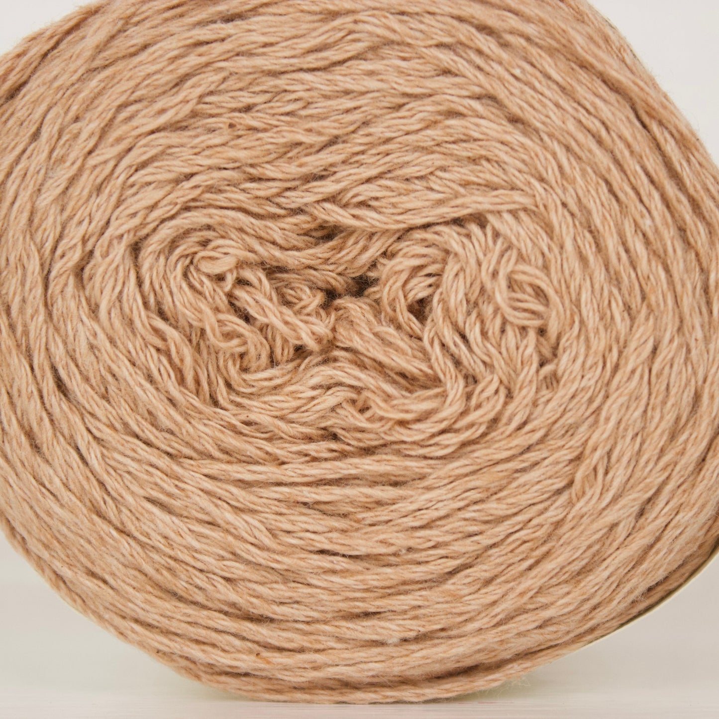 A ball of natural cotton in a warm tan color, photographed against a clean white background.