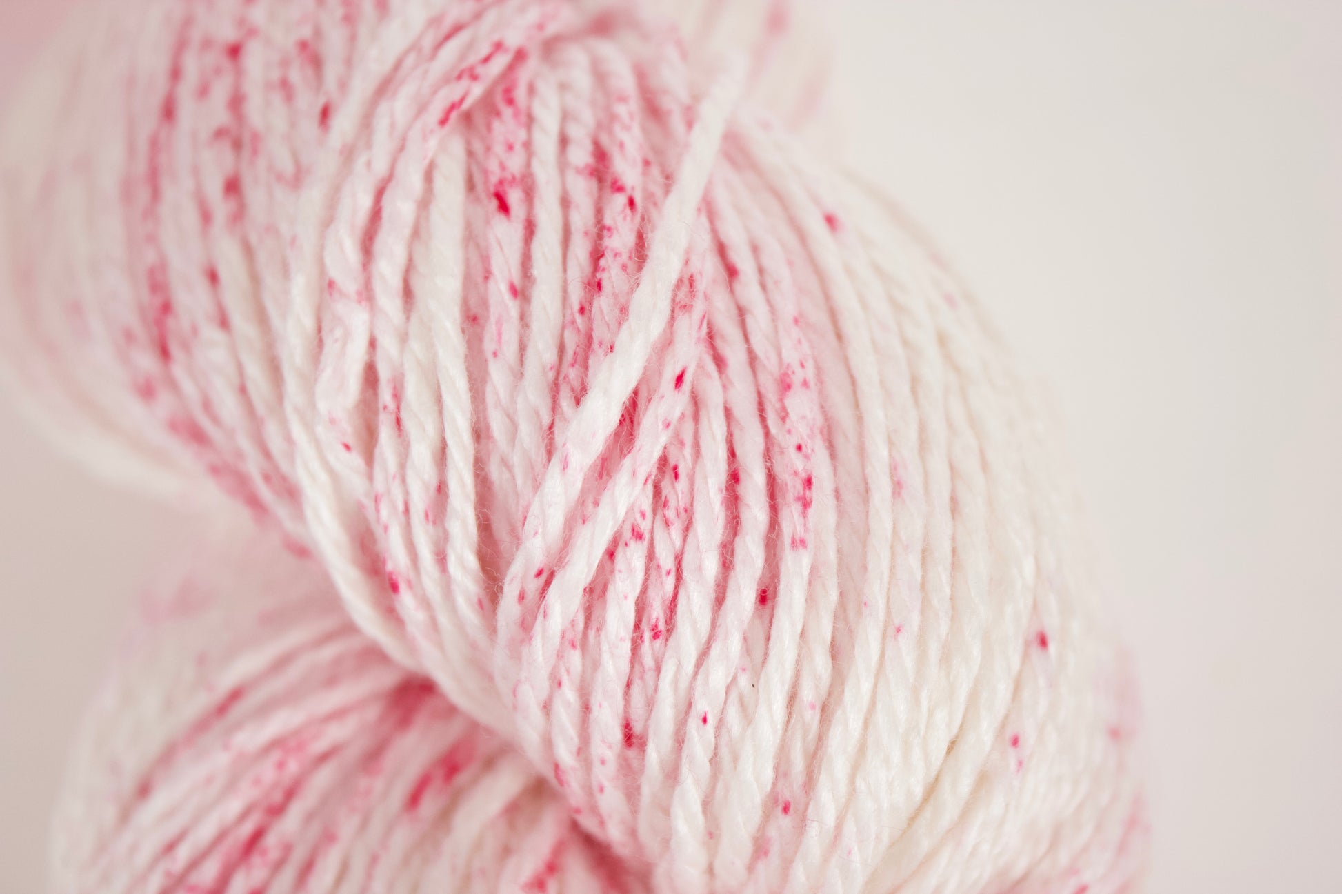 Raspberry Oat Mylk: Creamy white base with hot pink speckles in splotchy sections on Alnilam Worsted vegan yarn base.