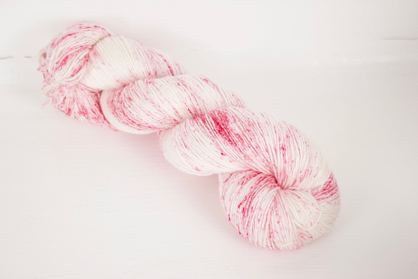 Raspberry Oat Mylk: Creamy white base with hot pink speckles in splotchy sections. Whole skein visible.
