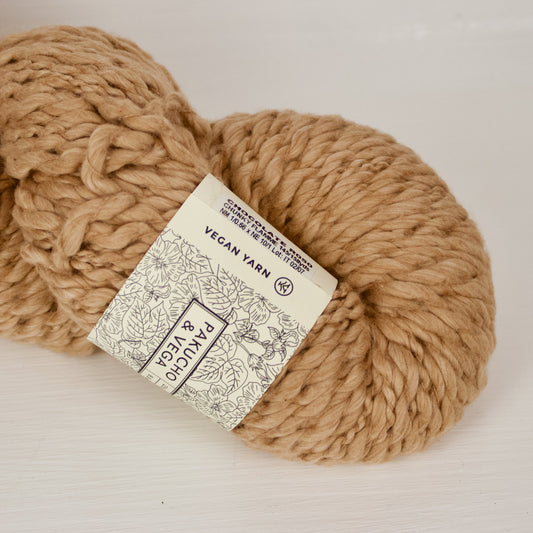Chocolate Vega x Pakucho is a thick and thin super bulky that's a natural warm light brown that's a little bit marled with cream. The skein is large and fluffy.