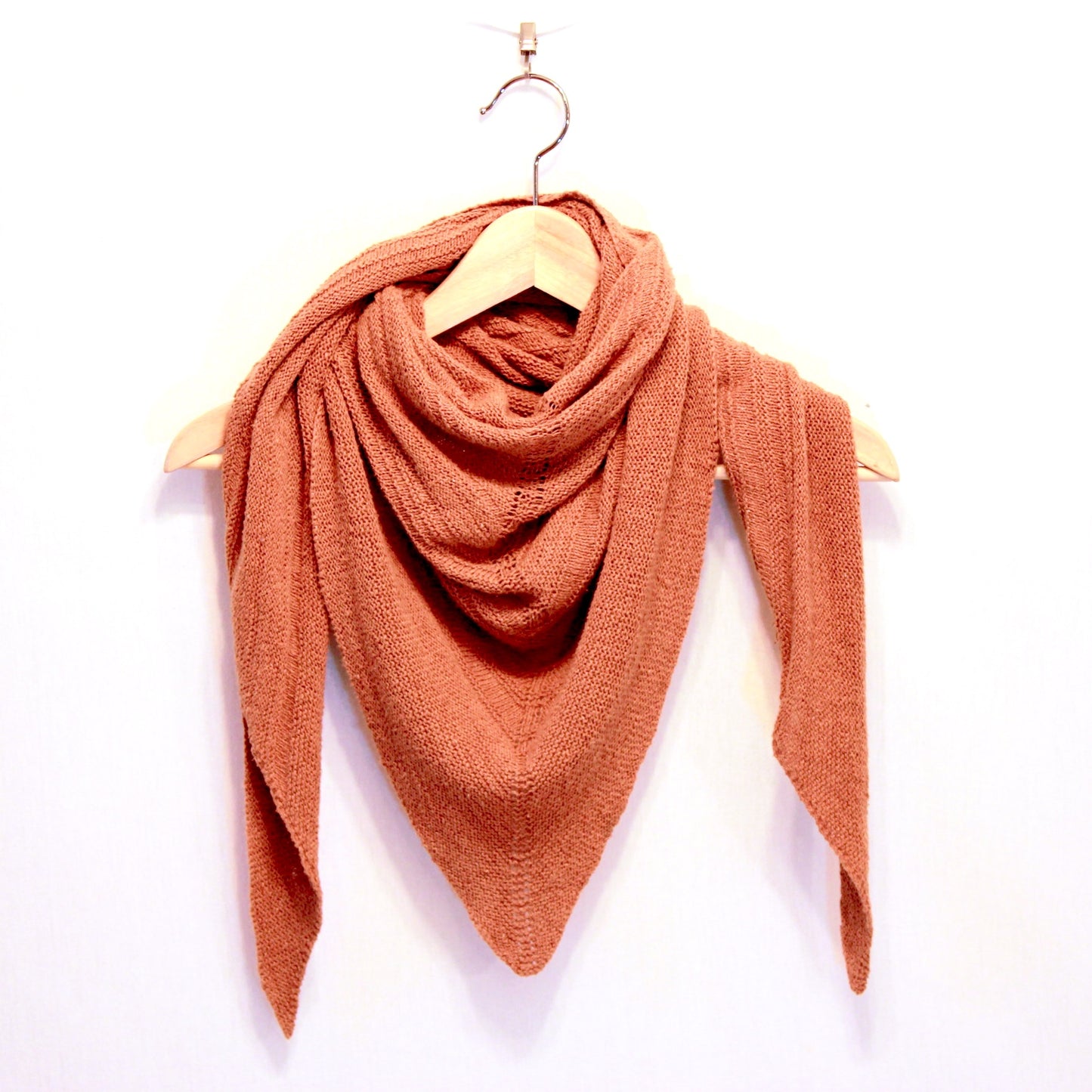 Deneb Shawl - Vegan Yarn - A generously sized triangular shawl wrapped kerchief style on a wooden hanger. Randomly alternating knit and purl rows create an organic texture on the surface that minimal and cozy. The colour is a warm ruddy brown made using Pakucho rust lace.
